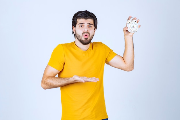 Free photo man holding an alarm clock and looks surprised.