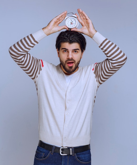 Man holding an alarm clock between palms.