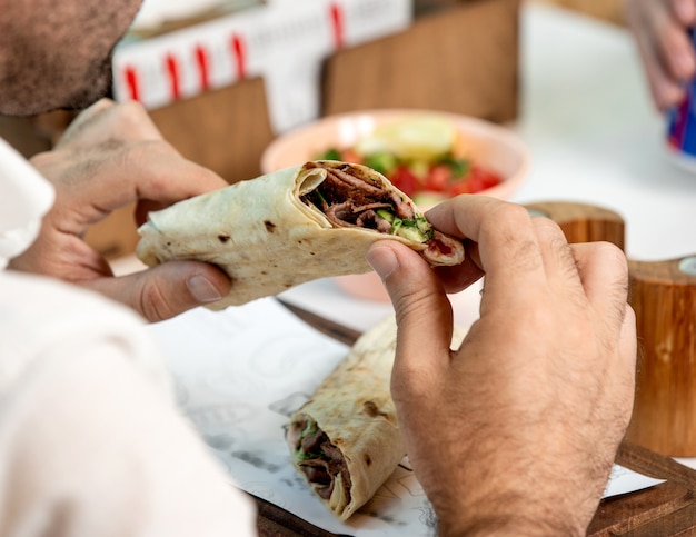 Man holding beef burger wrapped in flatbread