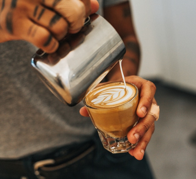 Free photo man holding a clear drinking glass with coffee and pouring the milk