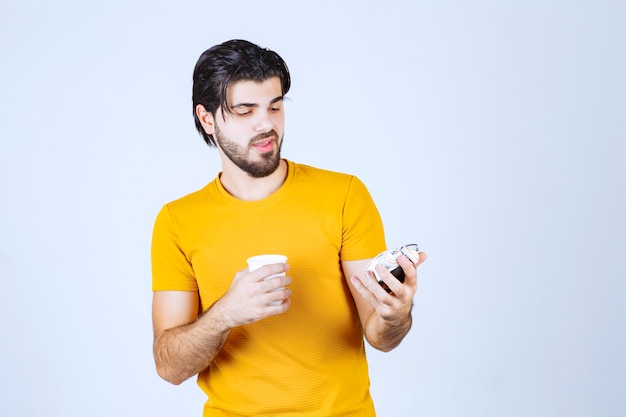 Free Photo man holding a coffee cup and alarm clock pointing to morning routine.