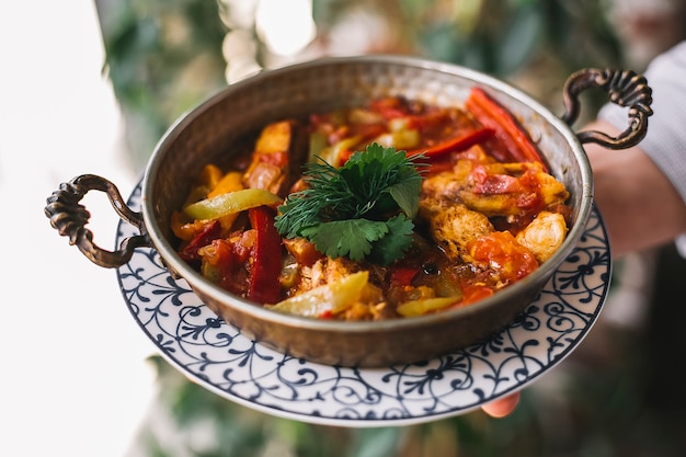 Free photo man holding a copper pan of sauteed chicken with green and red bell peppers