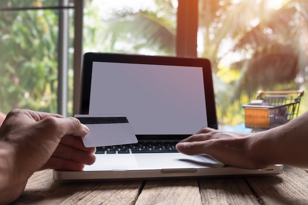 Man holding credit card in hand and entering security code using laptop keyboard