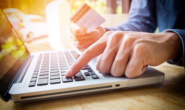 Free Photo man holding credit card in hand and entering security code using laptop keyboard.