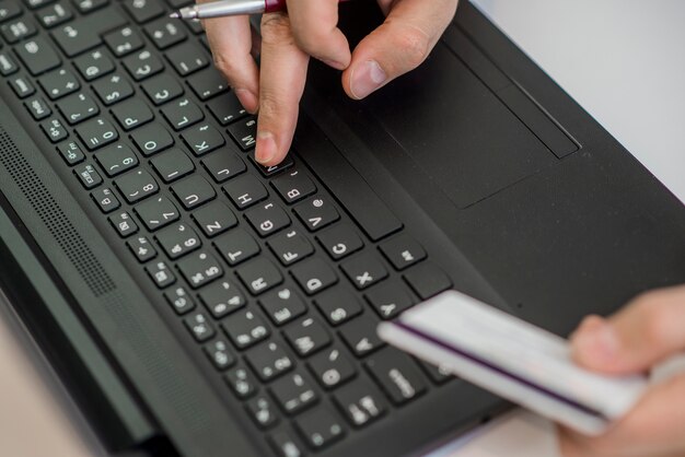 Man holding credit card in hand and entering security code using smart phone on laptop keyboard, online shopping concept.