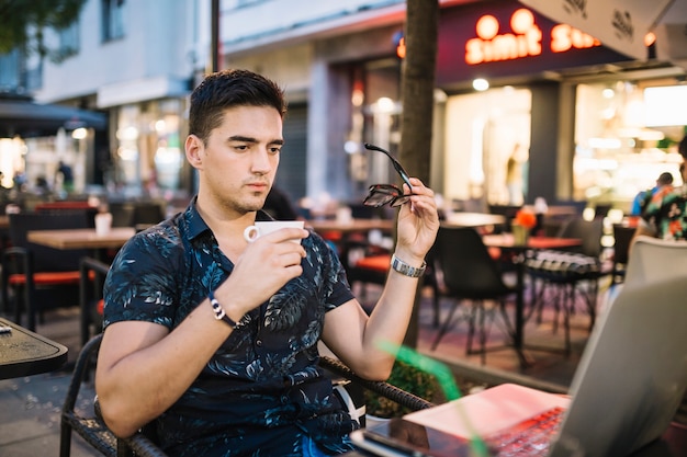 Man holding cup of coffee looking at laptop in caf�