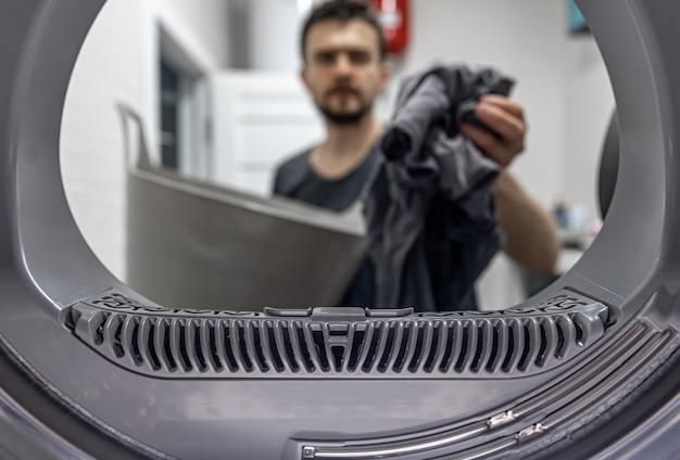 Man holding dirty cloth in hand view inside of washing machine.