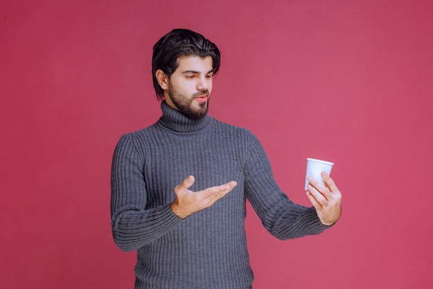 Man holding a disposable coffee cup and pointing at it.