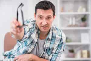 Free photo man holding eyeglasses in stretched out hand on chair at home