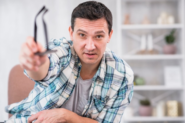 Free Photo man holding eyeglasses in stretched out hand on chair at home