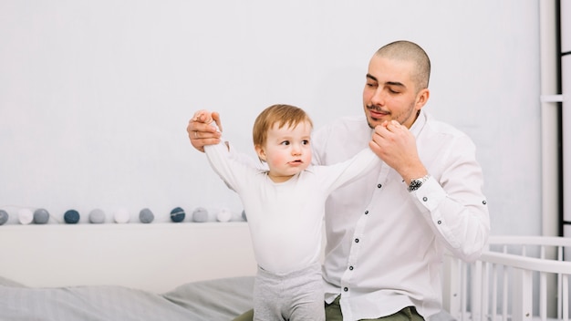 Free photo man holding hands of funny little baby on bed