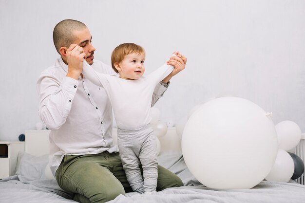 Free Photo man holding hands of little baby on bed