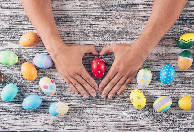 man holding heart shape with easter eggs on wooden background.