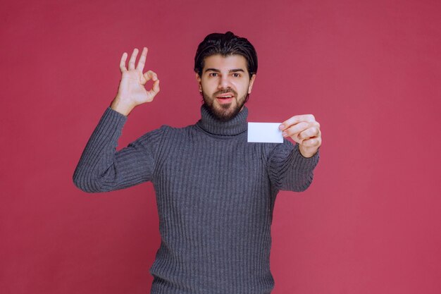 Man holding his business card and makes positive hand sign.