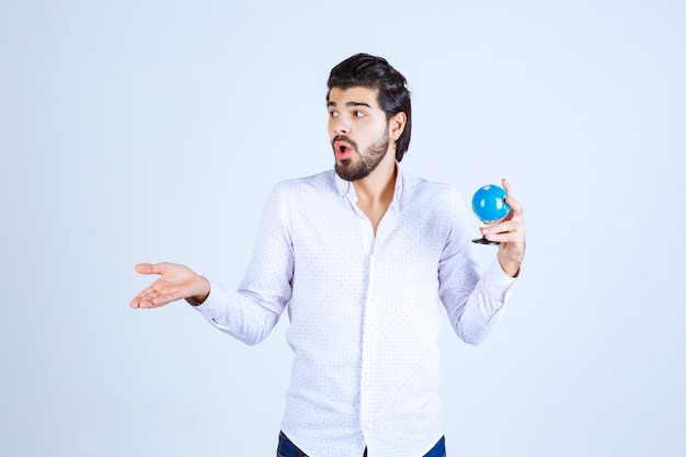 Free photo man holding a mini globe and looks confused