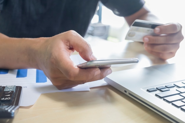 A man holding mobile phone and credit card on laptop for online shopping