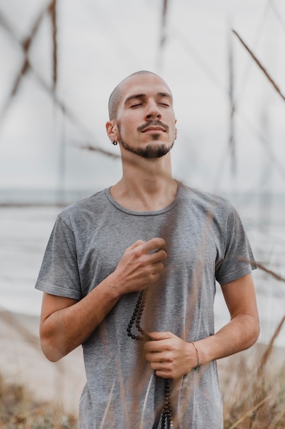 Free photo man holding rosary outdoors while doing yoga