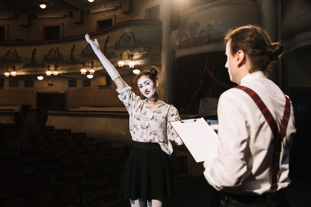 Free photo man holding scripts looking at female mime performing on stage