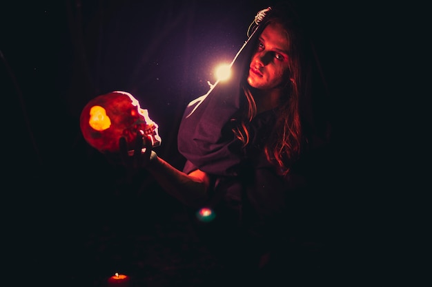 Free photo man holding a skull in the dark and looking at camera