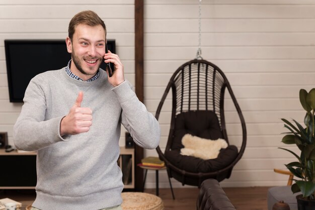 Man holding smartphone and giving thumbs up at home