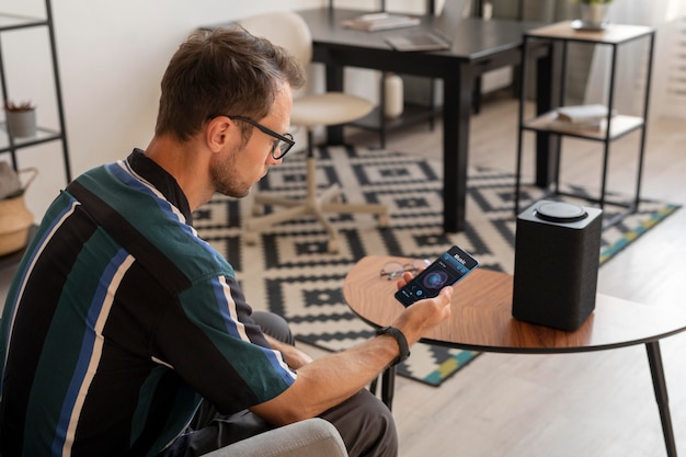 Free Photo man holding a smartphone while using a smart speaker