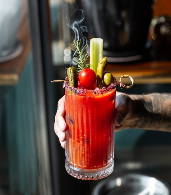 Man holding tomato juice garnished with celery stick olive pickled cucumber pepper