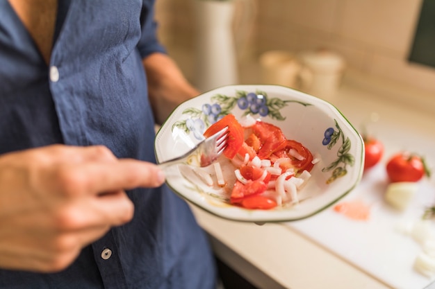 Man holding tomato slice with fork in the bowl