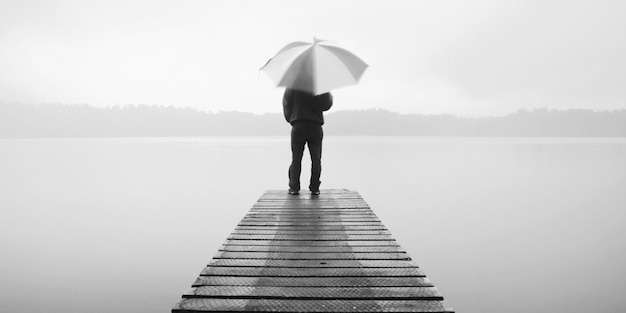 Free photo man holding an umbrella on a jetty by tranquil lake.