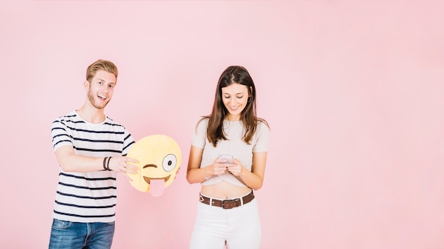 Free photo man holding winking eye emoji near smiling woman using cellphone