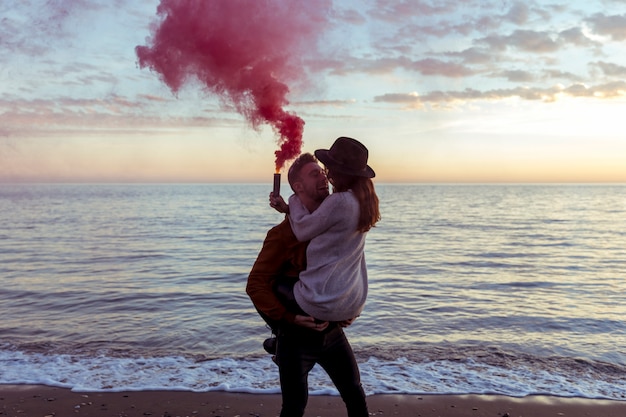 Free Photo man holding woman in arms with smoke bomb on sea shore 