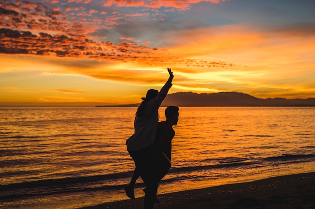 Free photo man holding woman on back on evening sea shore