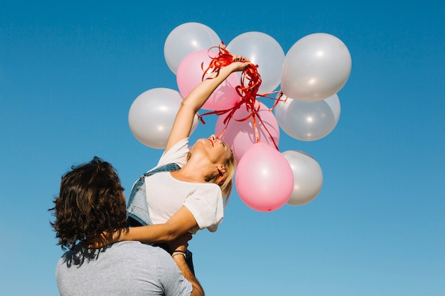 Free photo man holding woman with bunch of balloons