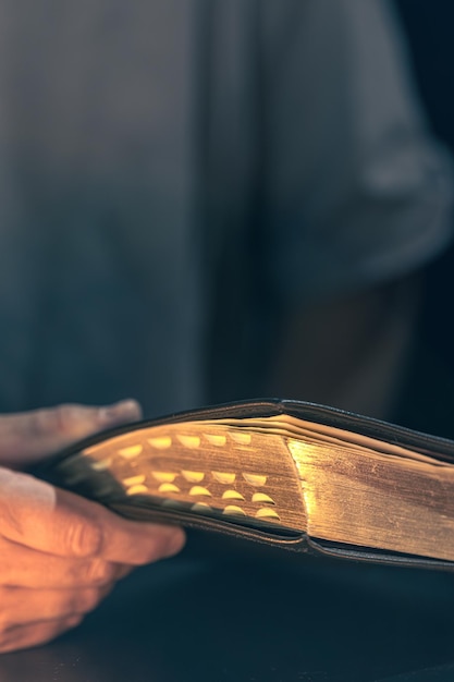 Free photo a man holds a bible in his hands bible with golden pages religion concept