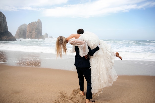 Man holds the woman on his shoulder and they are on the ocean beach