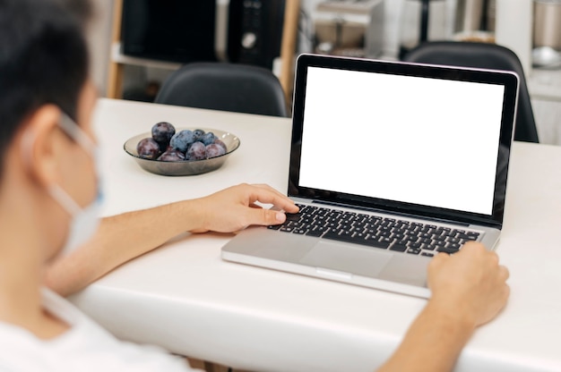 Man at home with medical mask during the pandemic and laptop