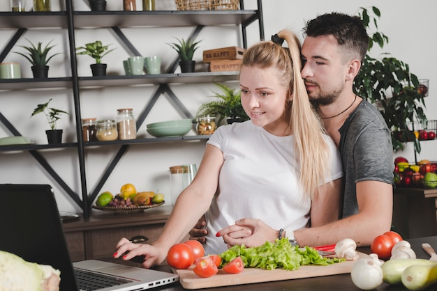 Free Photo man hugging her girlfriend using laptop white preparing food