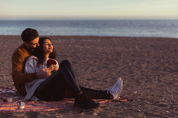 Free photo man hugging woman on coverlet on sea shore