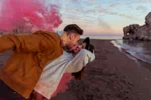 Free photo man hugging woman with pink smoke bomb on sea shore