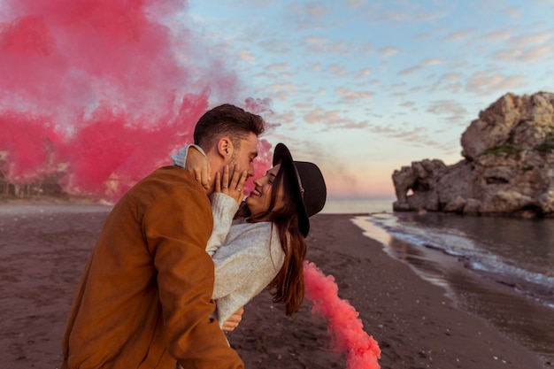 Free photo man hugging woman with smoke bomb on sea shore