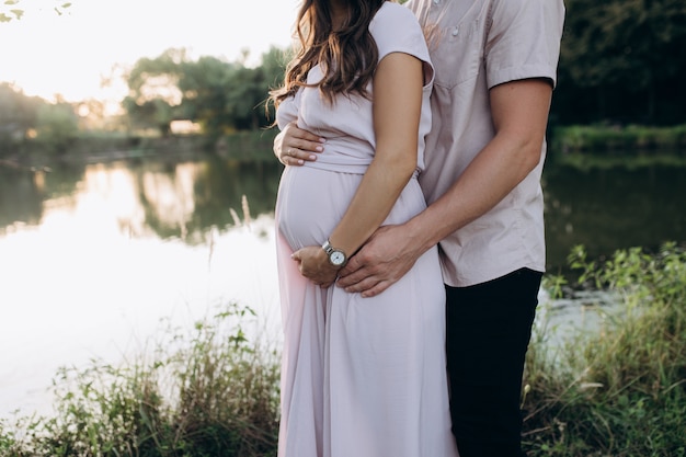 Free Photo man hugs beautiful pregnant woman tender standing before the lake