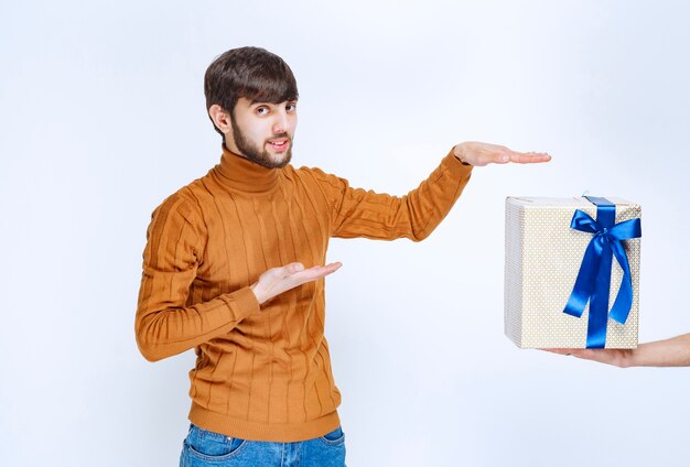 Man is being offered a white gift box with blue ribbon and he is pointing at it.