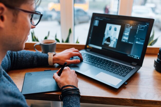 Man is editing photos on laptop, using graphics tablet and interactive pen display