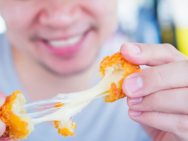 Man is going to eat sticky stretch fried cheese ball. 