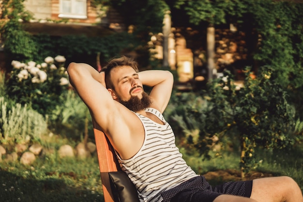 Free photo a man is resting in a country house. a bearded man enjoys the sunset on a green lawn.