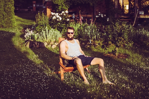 a man is resting in a country house. A bearded man enjoys the sunset on a green lawn.