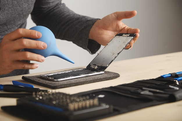 Free photo man is working carefully in his lab to repair and clean smart phone using syringe to blow out all dust from device