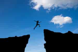 Free photo man jump through the gap between hill.man jumping over cliff on blue sky ,business concept idea