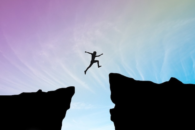 Man jump through the gap between hill.man jumping over cliff on sunset background,Business concept idea