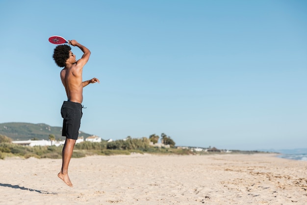 Man jumping with tennis racket on beach