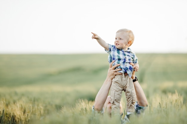 Man keeps the little boy above his head among the field